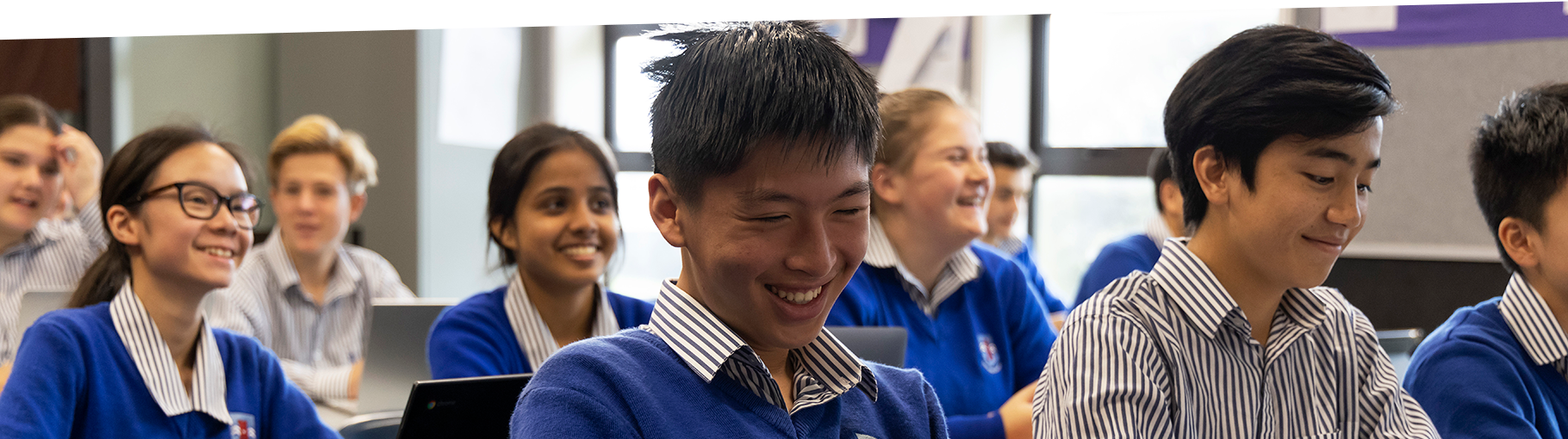 Macleans College students smiling in the classroom while working on laptops