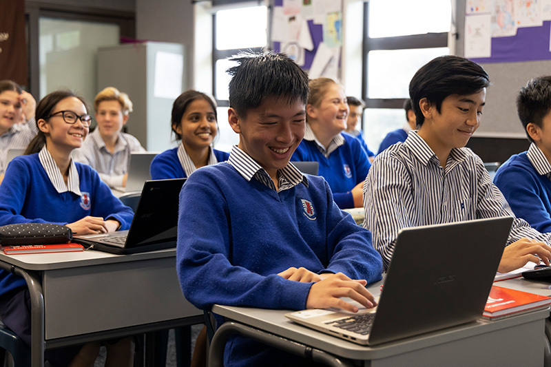 Macleans College students smiling in the classroom while working on laptops