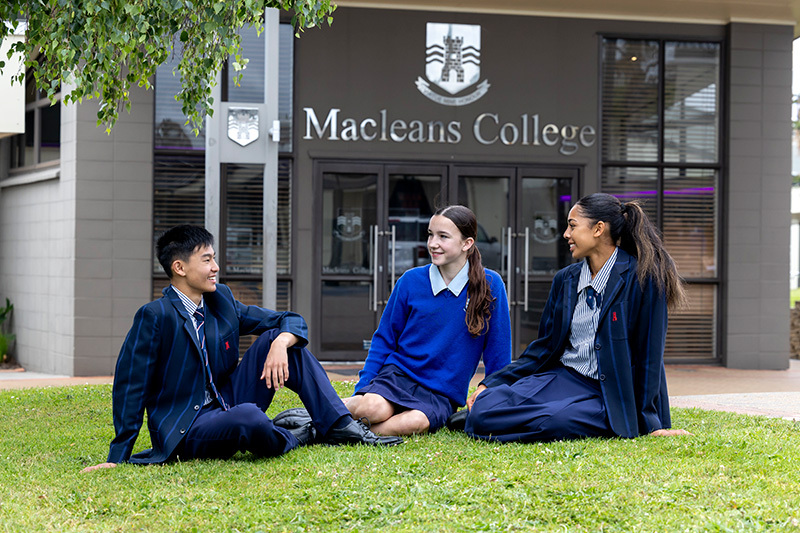 Macleans College students sitting under a tree in front of the school entrance